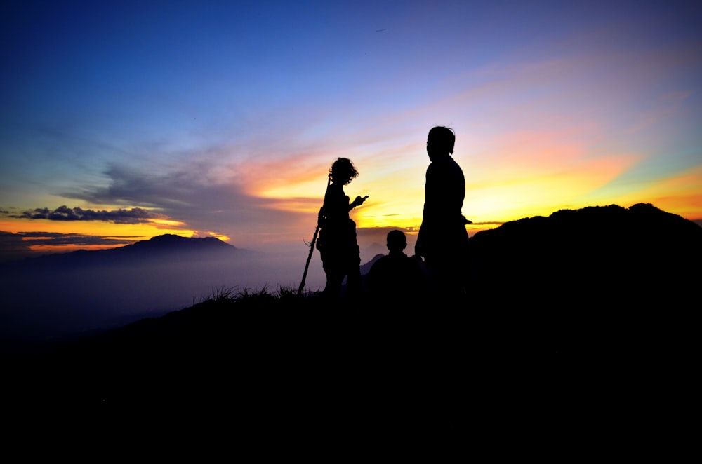 photographie de silhouette de trois personnes sur la montagne pendant l’heure dorée