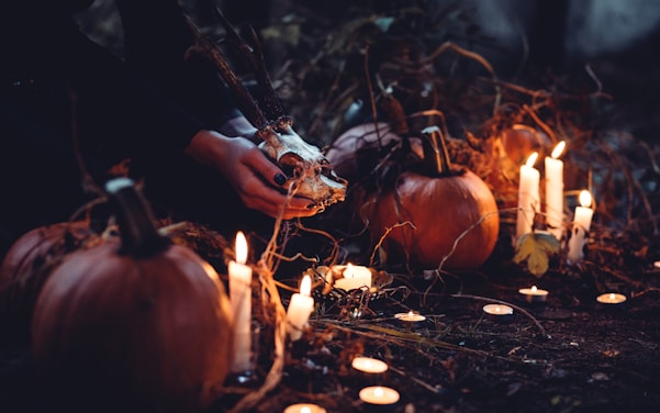 a photo of a person outside in the night, kneeling in front of pumpkins and lit candles