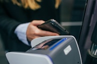 A person holding a smartphone near a contactless payment terminal, suggesting a digital transaction or payment process.