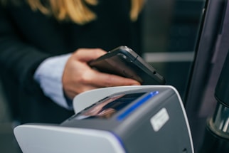A person holding a smartphone near a contactless payment terminal, suggesting a digital transaction or payment process.