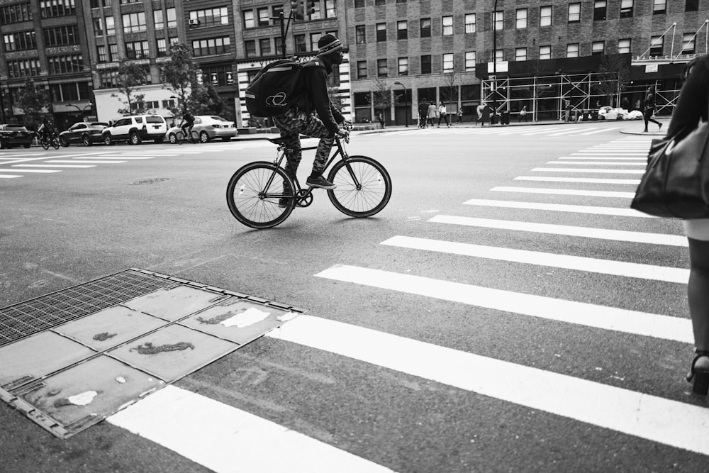 fotografia in scala di grigi dell'uomo che attraversa la corsia pedonale in bicicletta