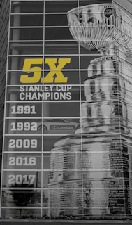 A large display features the image of the Stanley Cup and the text '5X Stanley Cup Champions' alongside the years 1991, 1992, 2009, 2016, and 2017. The display is on a glass building facade reflecting the environment, including a Lexus car and surrounding greenery.