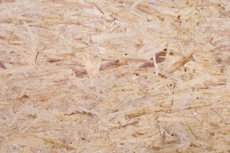 A close-up view of oriented strand board, showing an intricate pattern of compressed wood strands with a rough texture and varying shades of beige and brown.