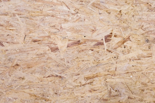 A close-up view of oriented strand board, showing an intricate pattern of compressed wood strands with a rough texture and varying shades of beige and brown.