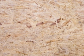 A close-up view of oriented strand board, showing an intricate pattern of compressed wood strands with a rough texture and varying shades of beige and brown.