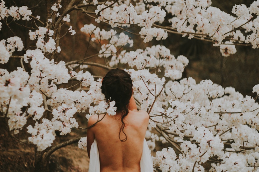 白い花びらの花のそばに立つトップレスの人