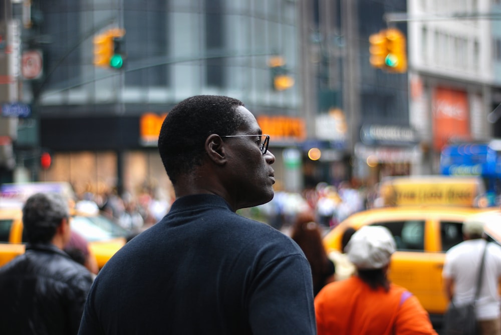 selective focus photography of man standing near road and buildings surrounded with crowd
