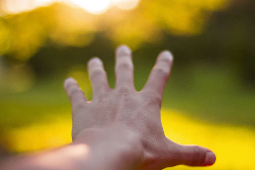 A blurred photo of a hand reaching out towards a glowing, elusive object.