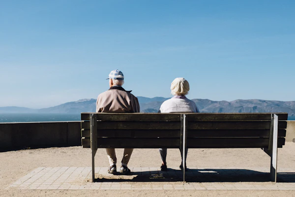 An older couple sitting on a bench looking out at the sea