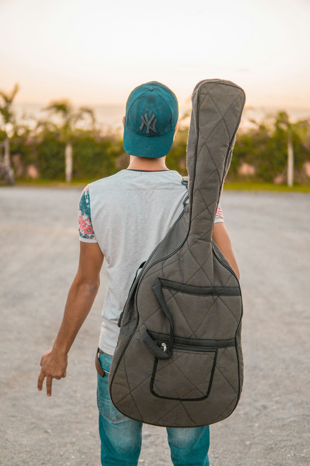 man looking at green trees carrying grey guitar case