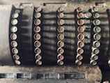 An old-fashioned, dusty cash register with multiple round keys displaying various monetary values. The keys are arranged in rows, featuring both numbers and words such as 'cash' and 'paid out.' The register has a worn, vintage appearance, indicating significant age and use.