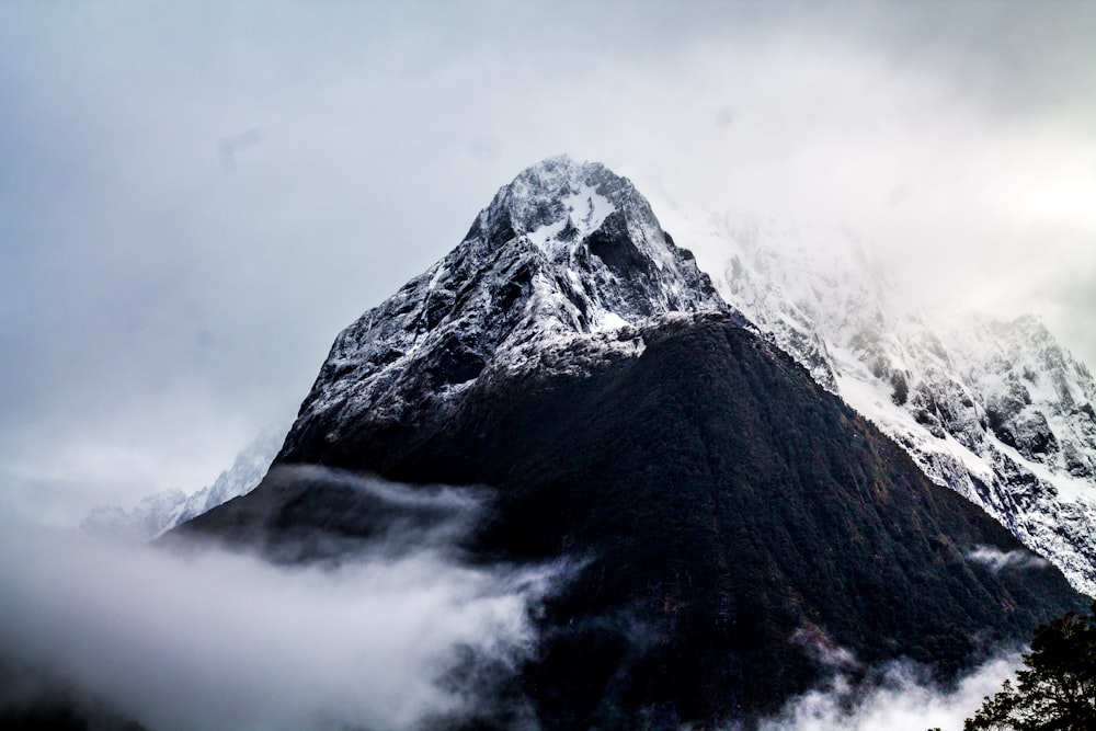 Montanha cinza e preta cercada por nevoeiro sob o céu branco durante o dia