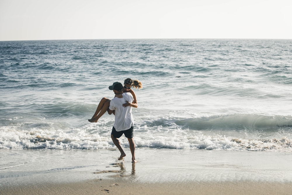 man carrying woman on seashore