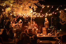 A warm evening scene of Porchlight Parade performing under soft porch lights, instruments in hand.