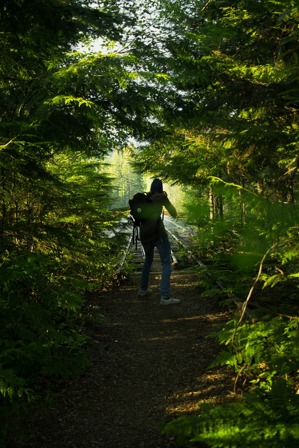 man in black jacket walking on pathway in between trees during daytime