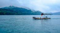 Traditional wooden boat sailing near the shore of Bali with lush green hills.