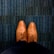 A pair of brown leather dress shoes is seen from an overhead perspective, resting on a textured blue carpet. The shoes are neatly laced and polished, showing detailed stitching and perforations.