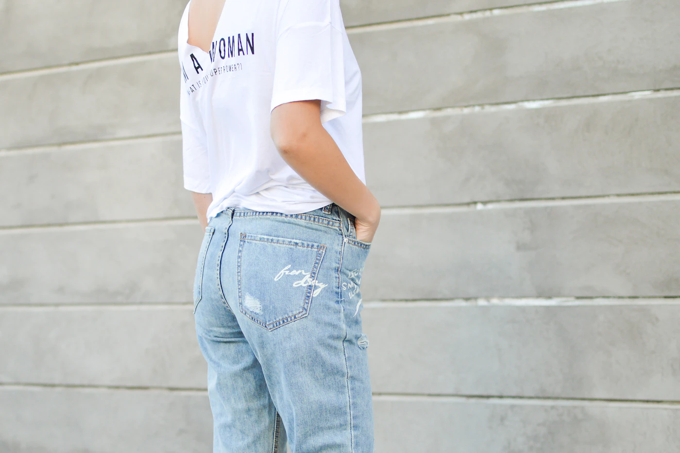 Woman in a white shirt and blue denim jeans standing against a wall, showing a simple everyday outfit