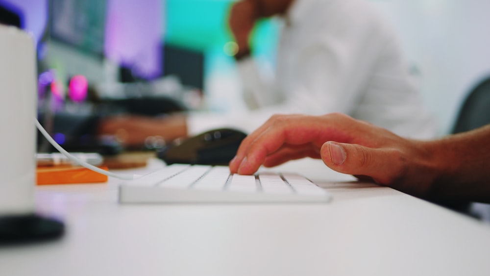 person holding white wireless computer keyboard on white wooden table inside room