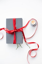 gray book wrapped with red ribbon beside teallight candle