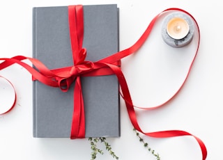 gray book wrapped with red ribbon beside teallight candle
