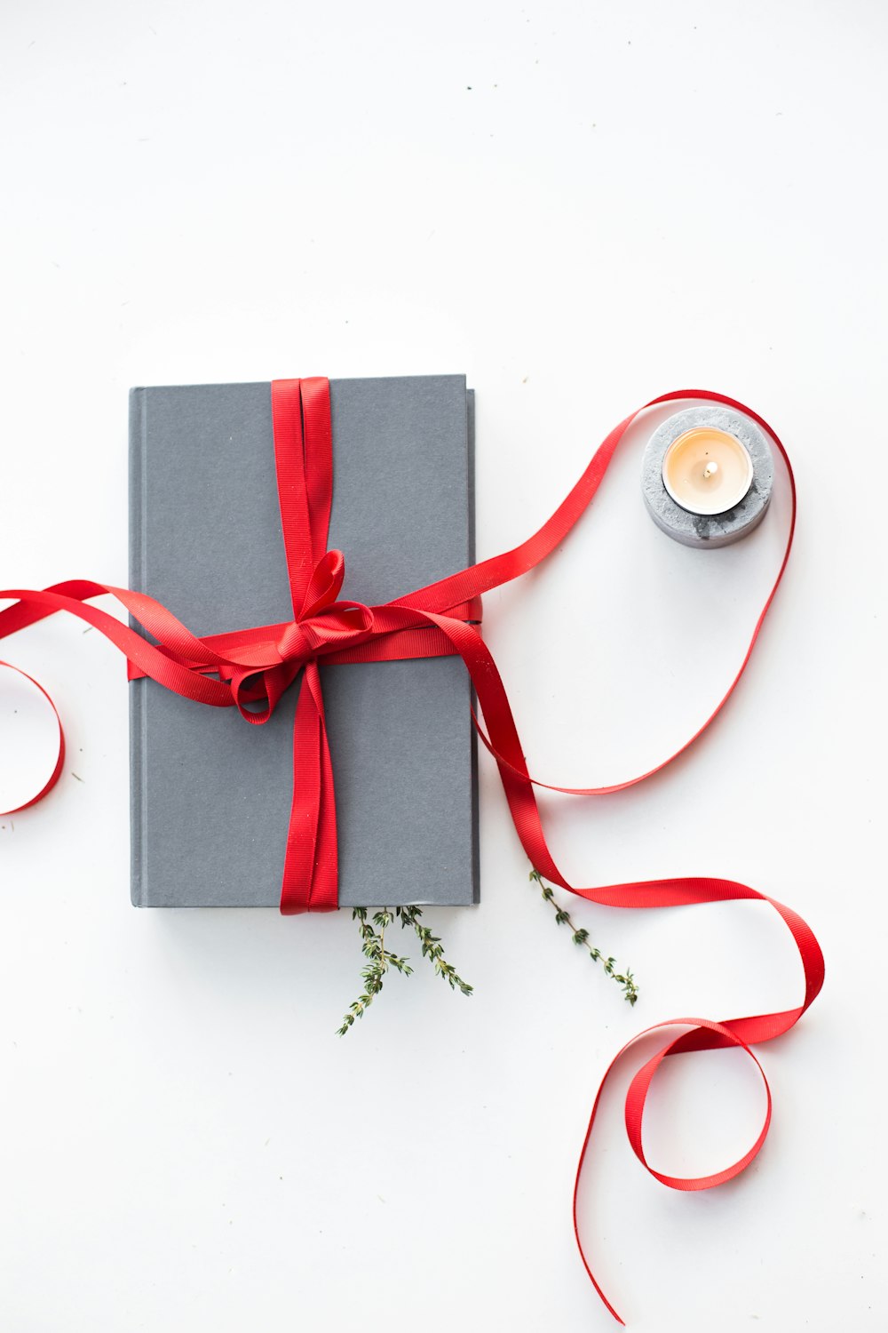 gray book wrapped with red ribbon beside teallight candle