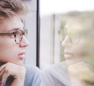 a man wearing glasses looking out a window