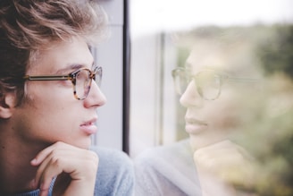 a man wearing glasses looking out a window