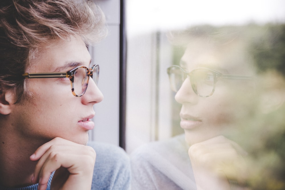 a man wearing glasses looking out a window