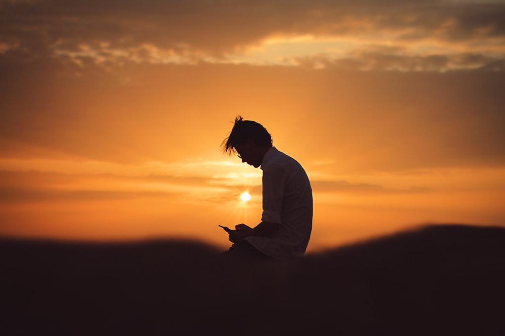 silhueta do homem usando o smartphone durante o pôr do sol