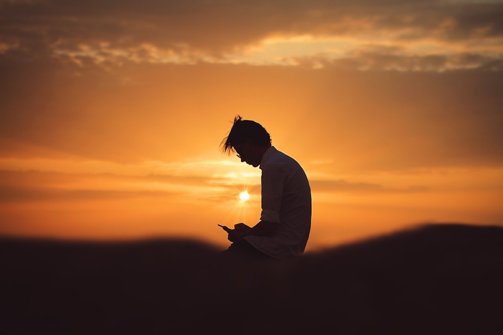Silueta de hombre usando teléfono inteligente durante la puesta del sol