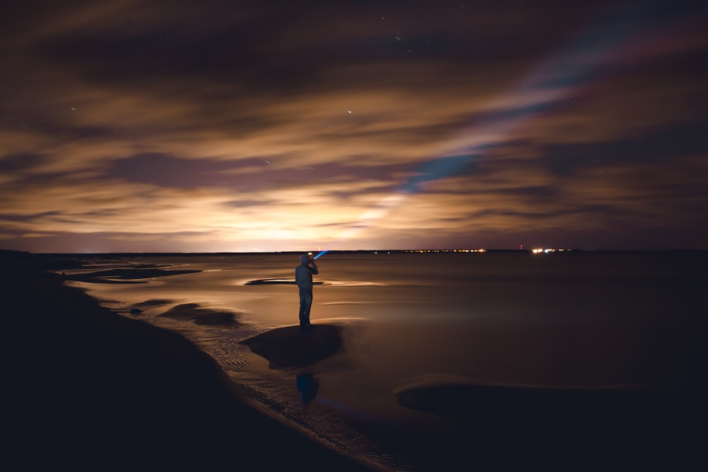 man standing on rock near body of water during golden hour