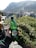 A plastic bottle labeled 'kiseljak' is held up by a hand, with a scenic background featuring a stone arch bridge and surrounding buildings and vegetation. Rolling hills and mountains rise in the distance under a clear sky.