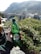 A plastic bottle labeled 'kiseljak' is held up by a hand, with a scenic background featuring a stone arch bridge and surrounding buildings and vegetation. Rolling hills and mountains rise in the distance under a clear sky.