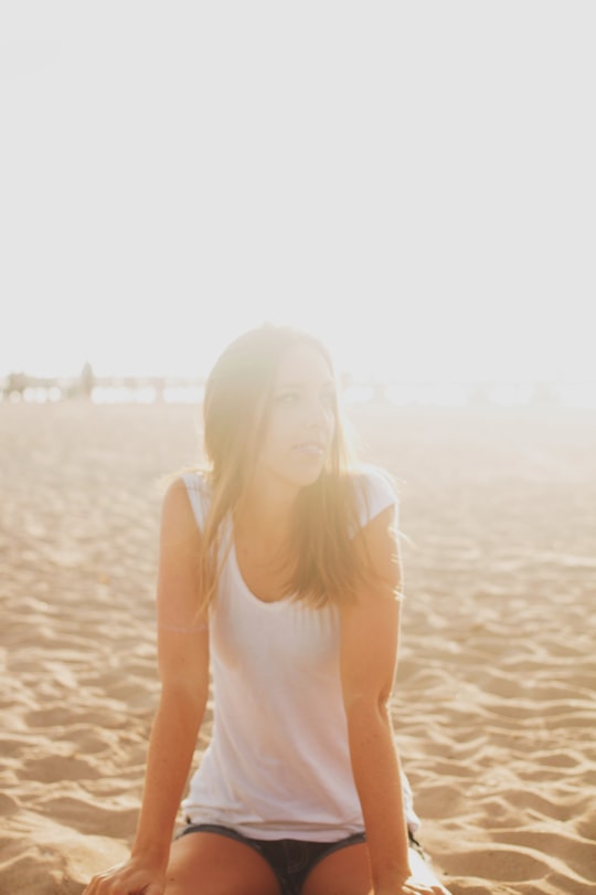 woman in white blouse sitting on brown sand in Huntington Beach United States