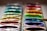 A close-up view of an open watercolor paint set with multiple vibrant colors arranged in a variety of hues. Each paint compartment is filled with wet paint, and a paintbrush is resting across one of the blue-colored sections on the right.