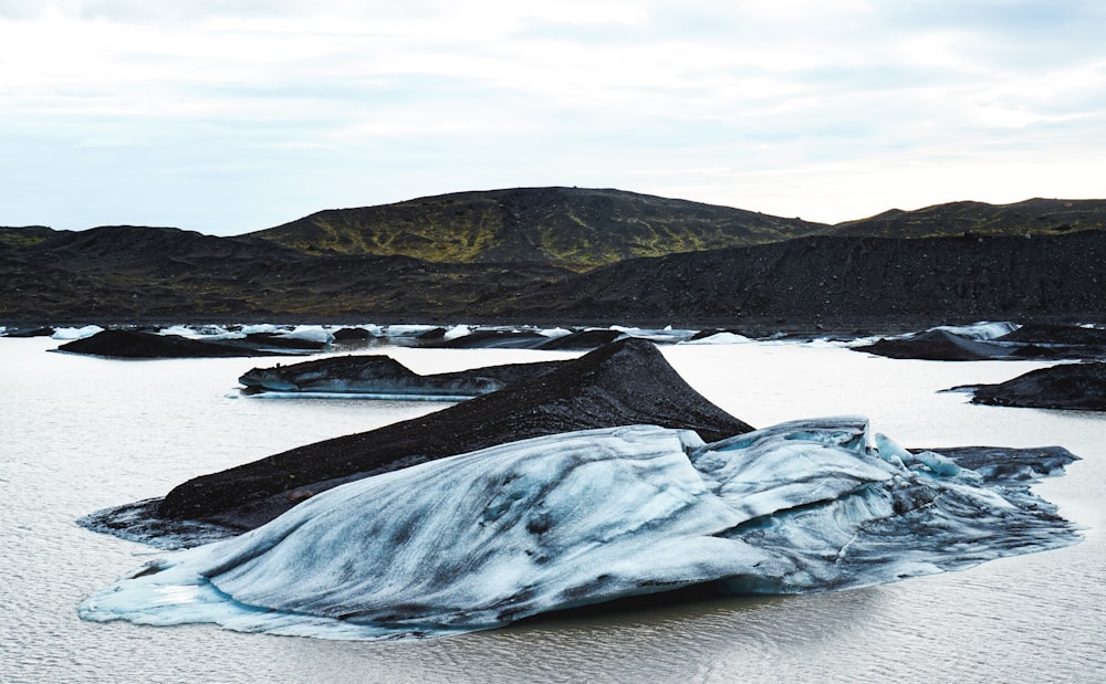 Schwarze und graue Hügel in der Nähe eines Gewässers unter blauem Himmel