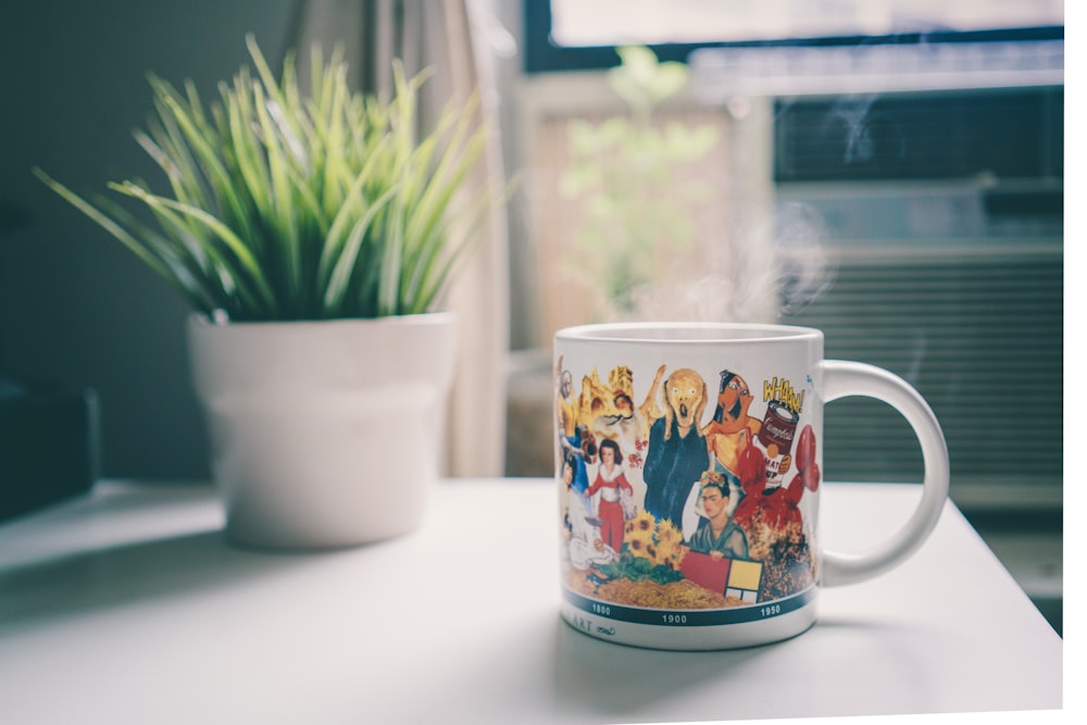 shallow focus photography of white ceramic mug beside green leafed plant