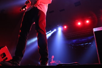 R J Yadav performing on stage with a microphone under cinematic lighting.