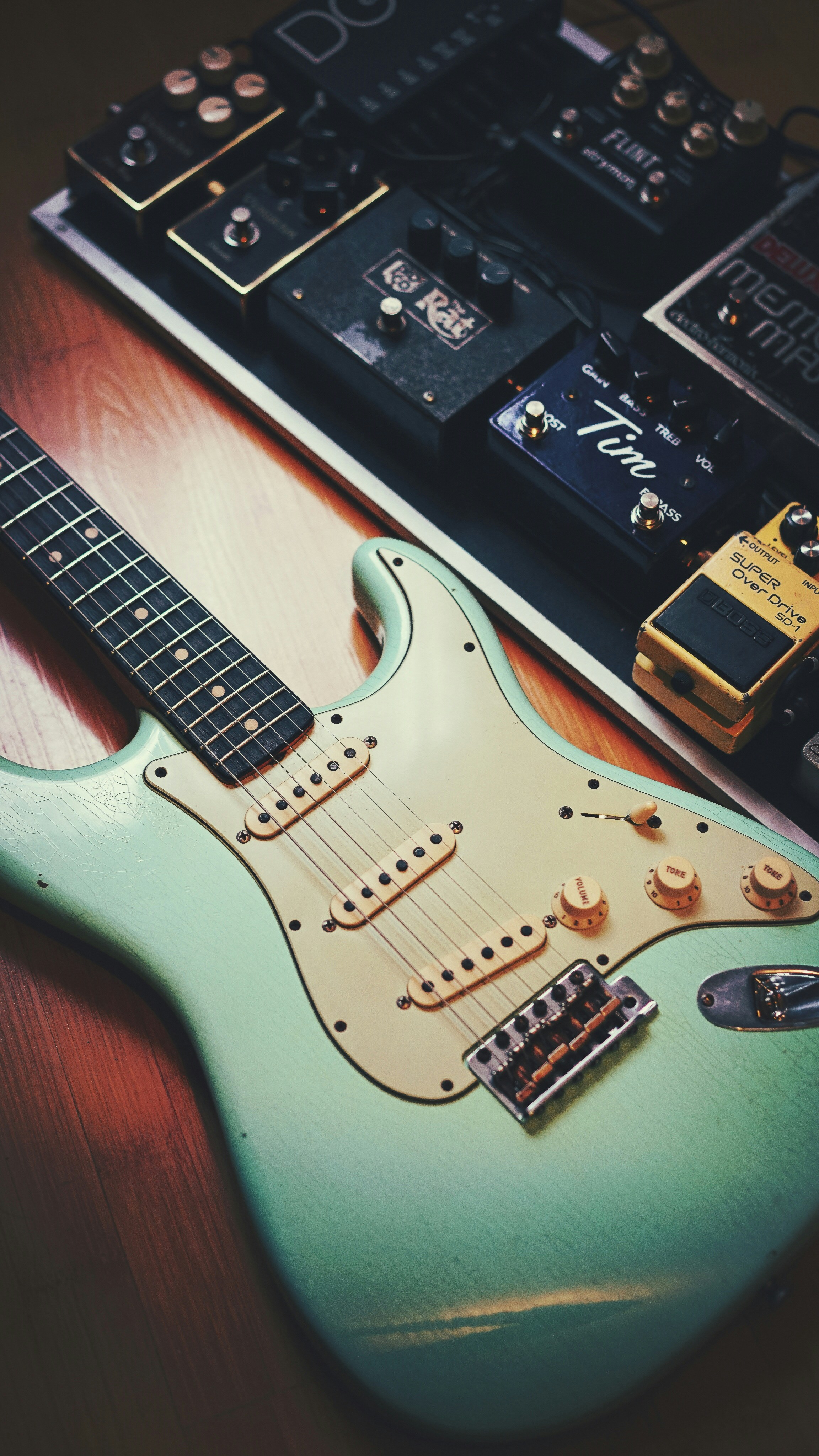 A seafood green Stratocaster placed on the floor with guitar pedals.