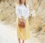 woman holding brown leather 2-way bag standing near grey rocky mountain