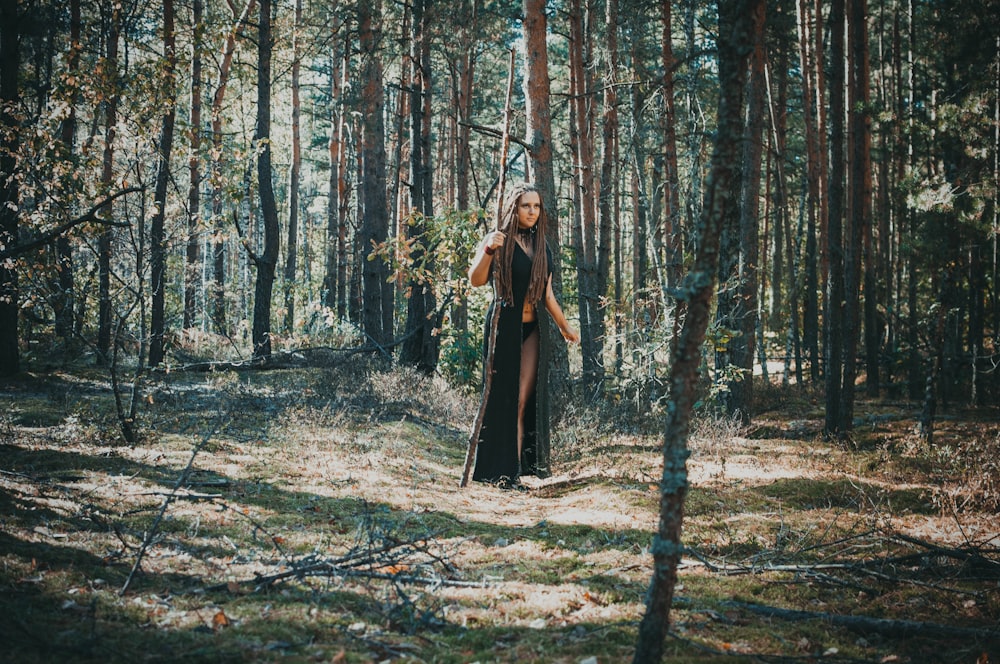 woman wearing black robe holding stick in the forest