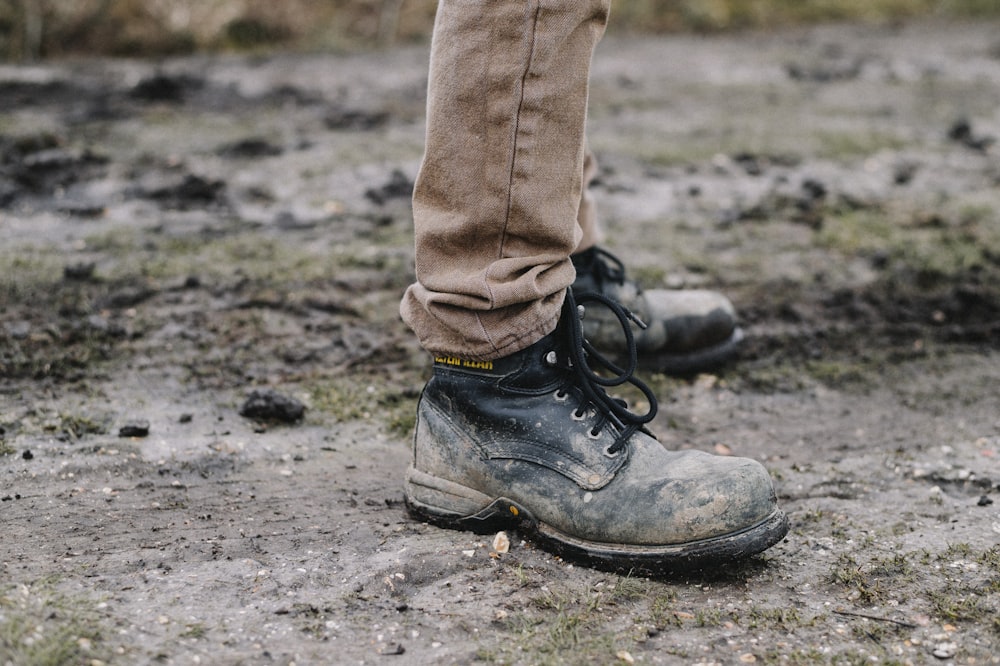 person in black work shoes standing on dirt pathway