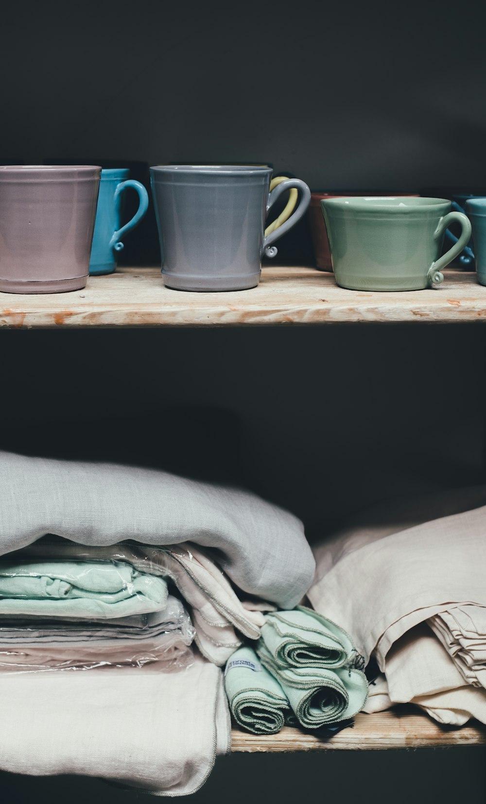 assorted-color ceramic mugs on top of shelf above piles of textile