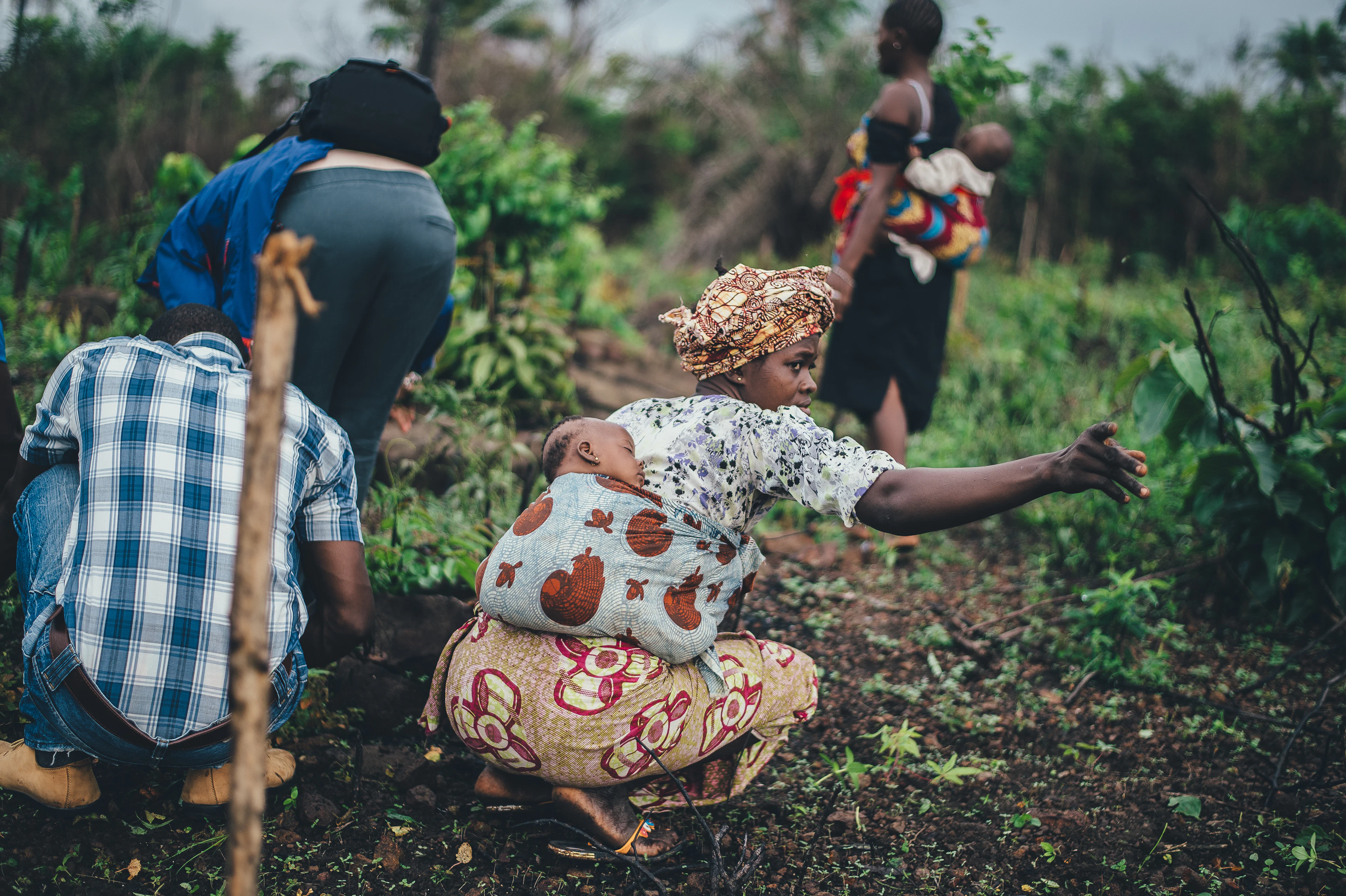 Women working a farm plot, one with her baby tied to her back