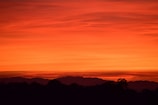Silhouetted mountains beneath a vibrant orange-and-red sky at sunset.