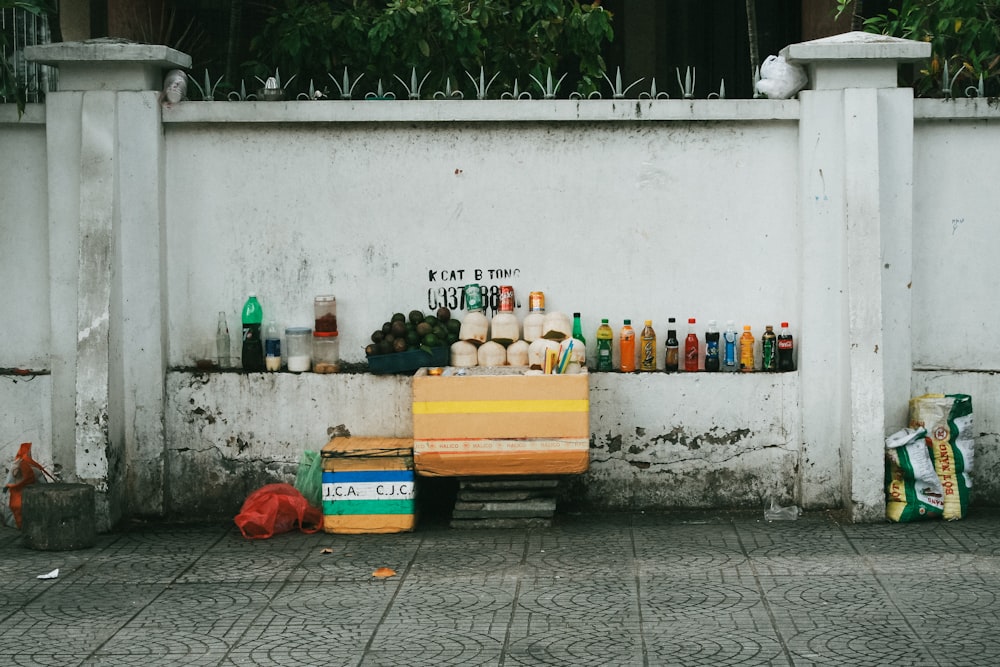 assorted-labeled bottle display on white concrete wall near gray pavement at daytime