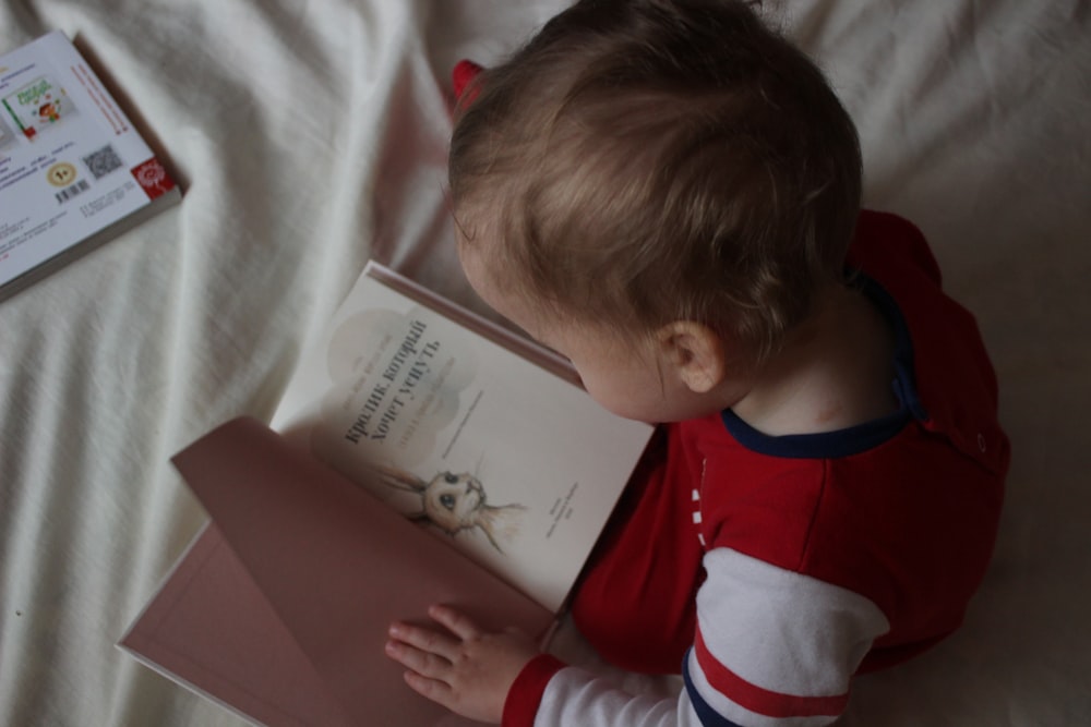 baby sitting on bed while reading on book