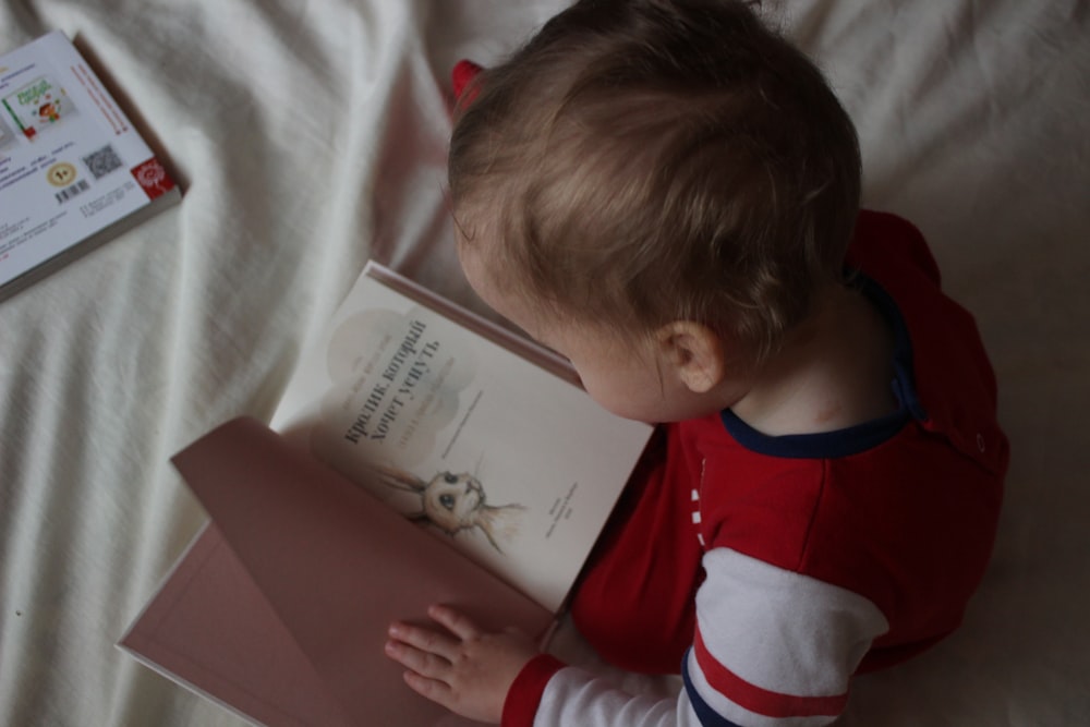 침대에 앉아서 책을 읽는 아기