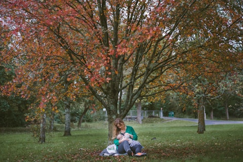woman holding baby sitting under the tree